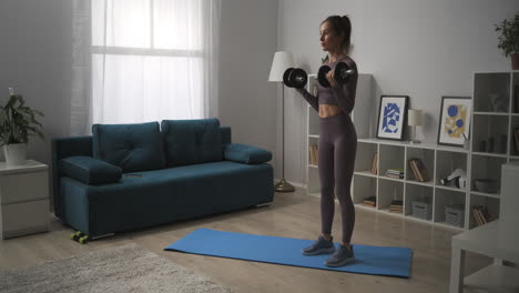 slim-woman-is-lifting-dumbbells-in-living-room-training-biceps-home-for-good-shape-of-body-home-daily-training-in-apartment-fitness-and-wellness-healthy-lifestyle